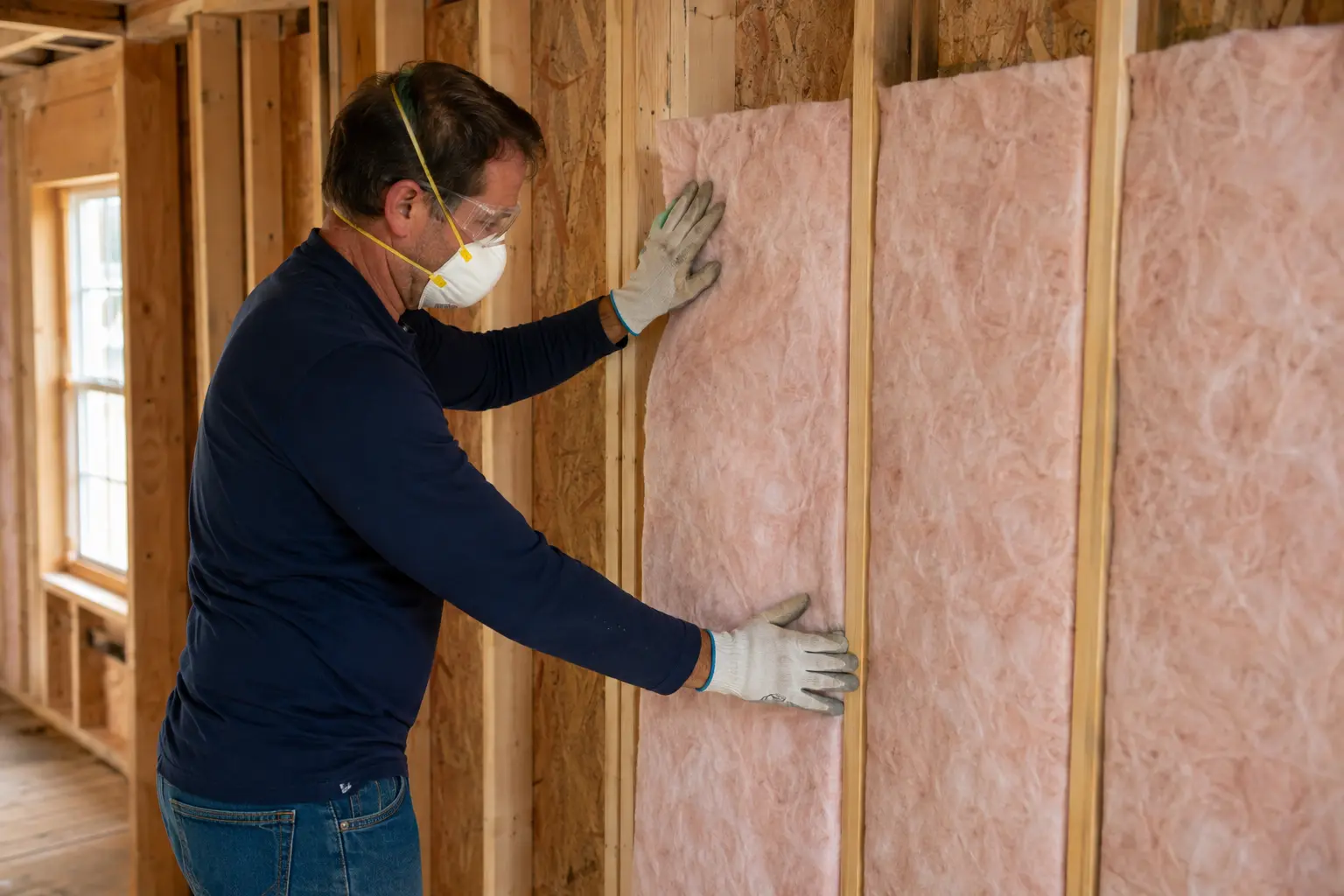 Installer precisely fitting fiberglass batt insulation between open wall studs